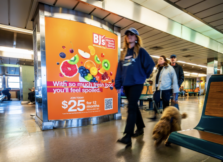 Woman walking with her dog in front of an advertisement of BJs Wholesale inside the Staten Island Ferry